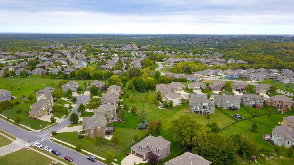 drone view of a neighbourhood full of gyet houses with green trees and lawn.