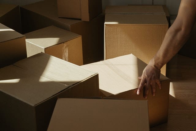 person's arm grabbing a box  amongst a pile of boxes for blog post how to move out of your parents house