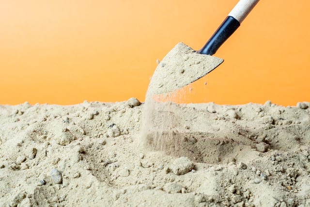 shovel scooping sand, on an orange background, to be placed in sandbags used to build a flood wall