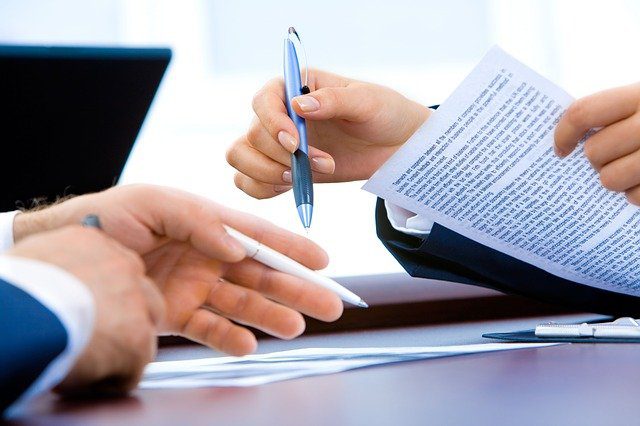 close-up of a buyer and lender both holding pens and documents working to stop a foreclosure at a property the last minute