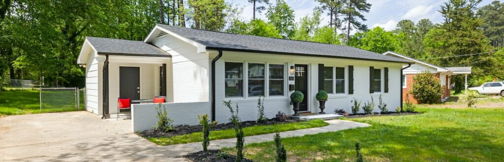 front of a beautiful family house with a gray roof and white walls surrounded by a green lawn and trees after renovation by Veritas Buyers in Alabama.